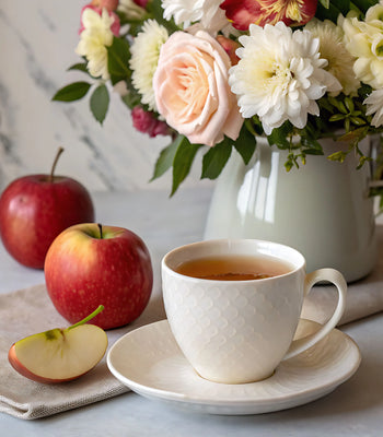 Cup of apple rose tea beside fresh apples and flowers on a table
