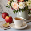 Cup of apple rose tea beside fresh apples and flowers on a table