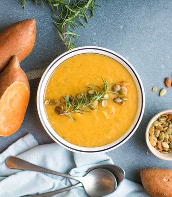 Top-down view of creamy curried carrot and sweet potato soup topped with seeds and rosemary.