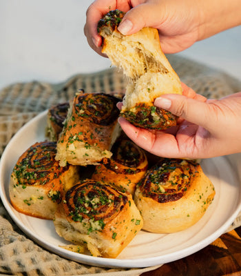 Hands pulling apart a soft, cheesy garlic butter swirled roll on a white serving plate