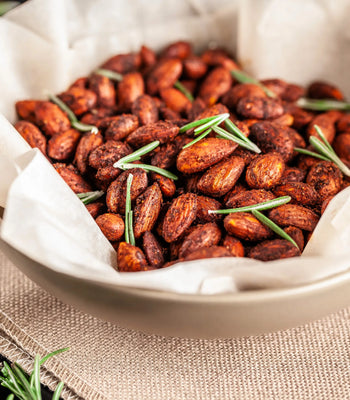 Roasted almonds seasoned with chili spices and fresh rosemary in a parchment-lined bow
