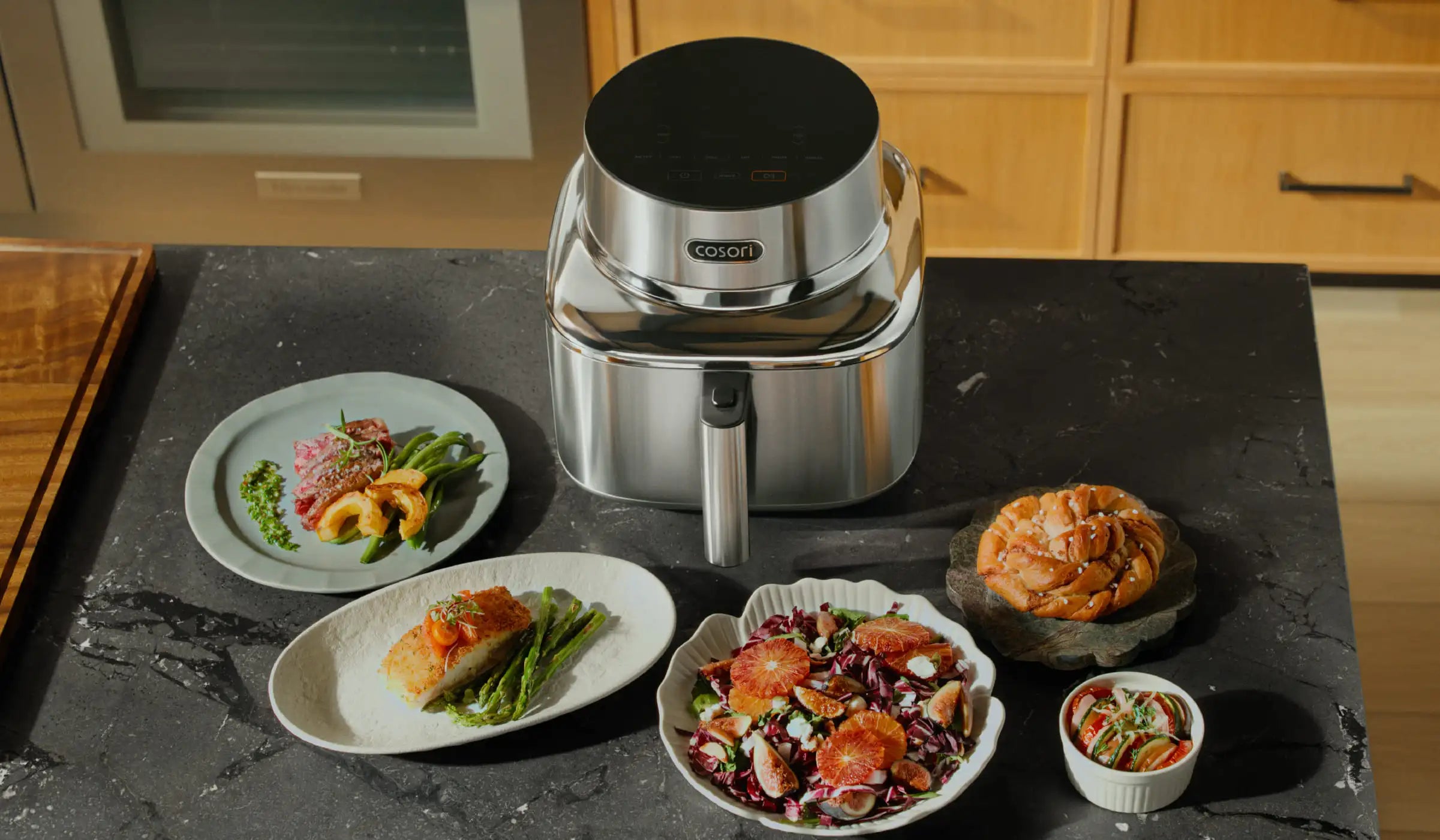 A sleek Cosori air fryer on a kitchen countertop surrounded by plates of freshly cooked food, representing easy everyday cooking.