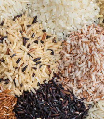 Piles of various raw rice types, including white, brown, red, and black grains, showcasing diverse colors.