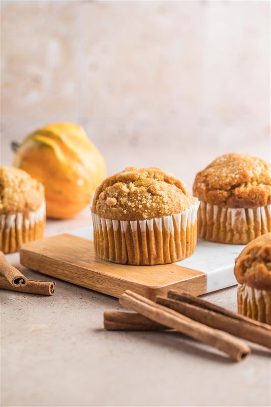 Gluten-free pumpkin spice cupcakes with crumb topping on a board with cinnamon sticks.