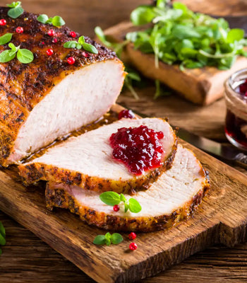 Sliced roasted pork loin topped with cranberry sauce and fresh herbs on a wooden board.