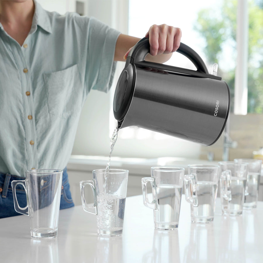 Person pouring hot water from COSORI Double-Wall Stainless Steel Electric Kettle into cups