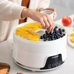 Person placing fresh fruit onto trays of COSORI Pioneer 5-Tray Food Dehydrator